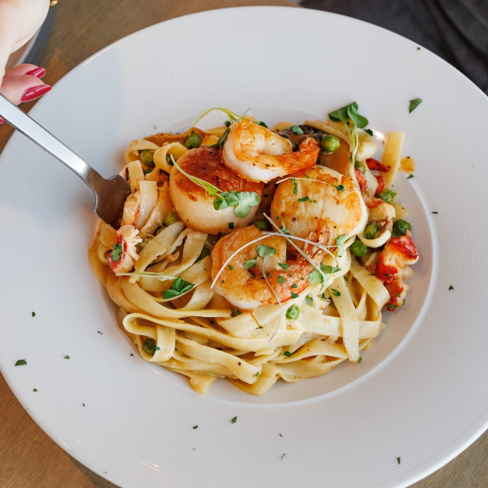 Creamy fettuccine pasta with shrimp, scallops, lobster, and peas, garnished with microgreens.