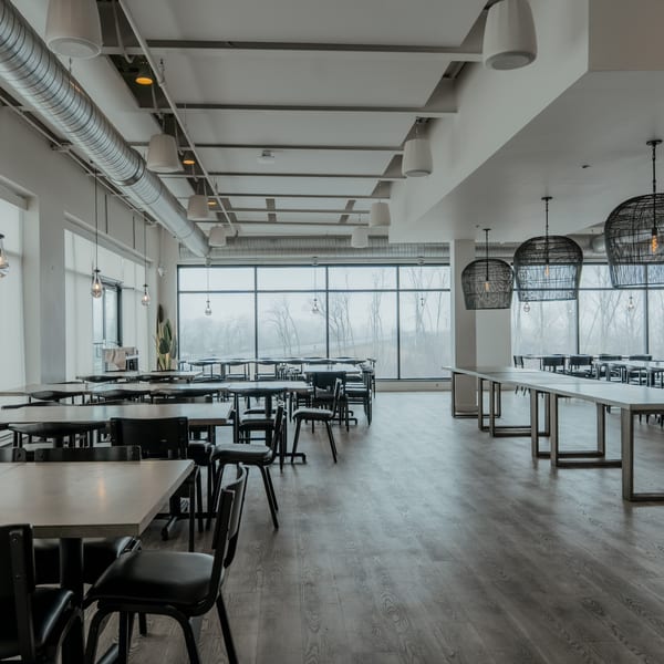 Spacious, modern dining room with long tables, black chairs, and large windows overlooking a misty landscape.