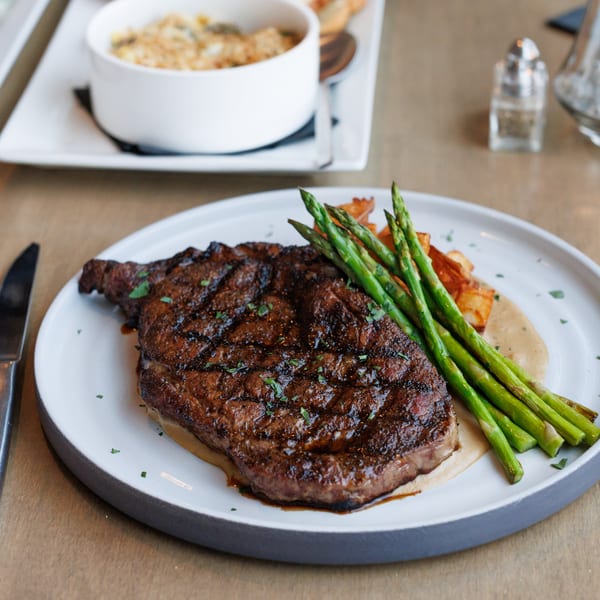 Grilled steak with asparagus and a side of mac and cheese on a white plate.
