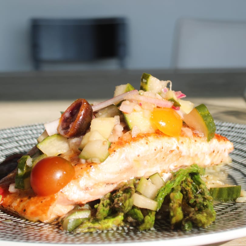 Grilled salmon fillet topped with fresh cucumber, tomato, and olive salsa, served with asparagus.