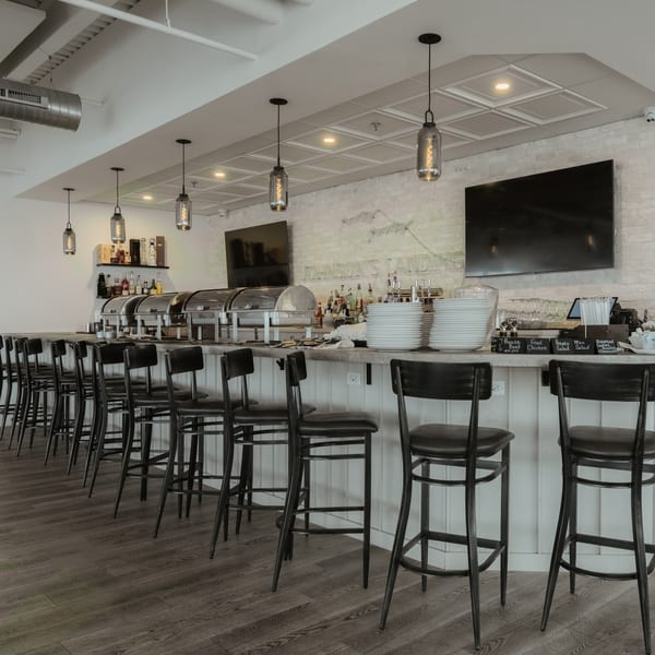 A long bar with black stools, buffet warmers, stacked plates, and menu signs at Johnson's Landing.