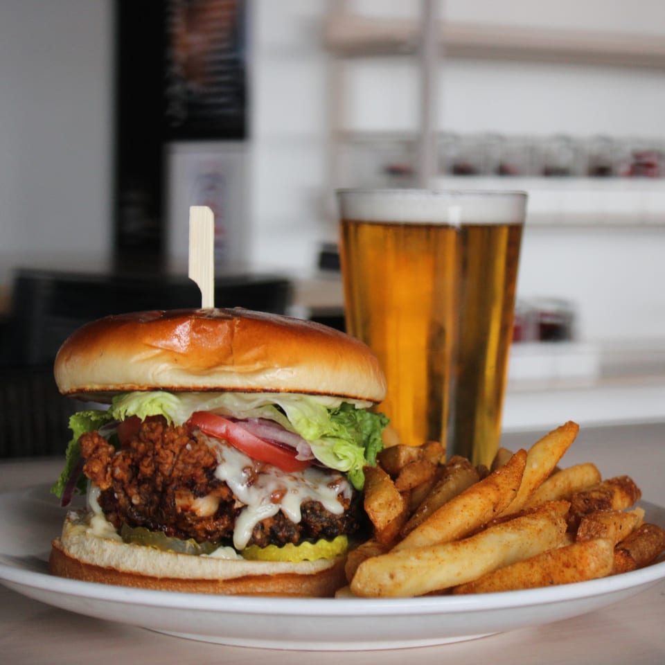 Crispy chicken sandwich with melted cheese, lettuce, tomato, pickles, fries, and a beer.