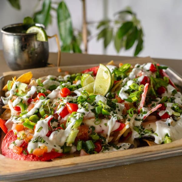 Loaded nachos with red and yellow chips, white sauce, green onions, red peppers, and lime.