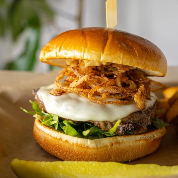 Johnson's Landing burger with melted cheese, crispy onions, arugula, and a pickle spear.